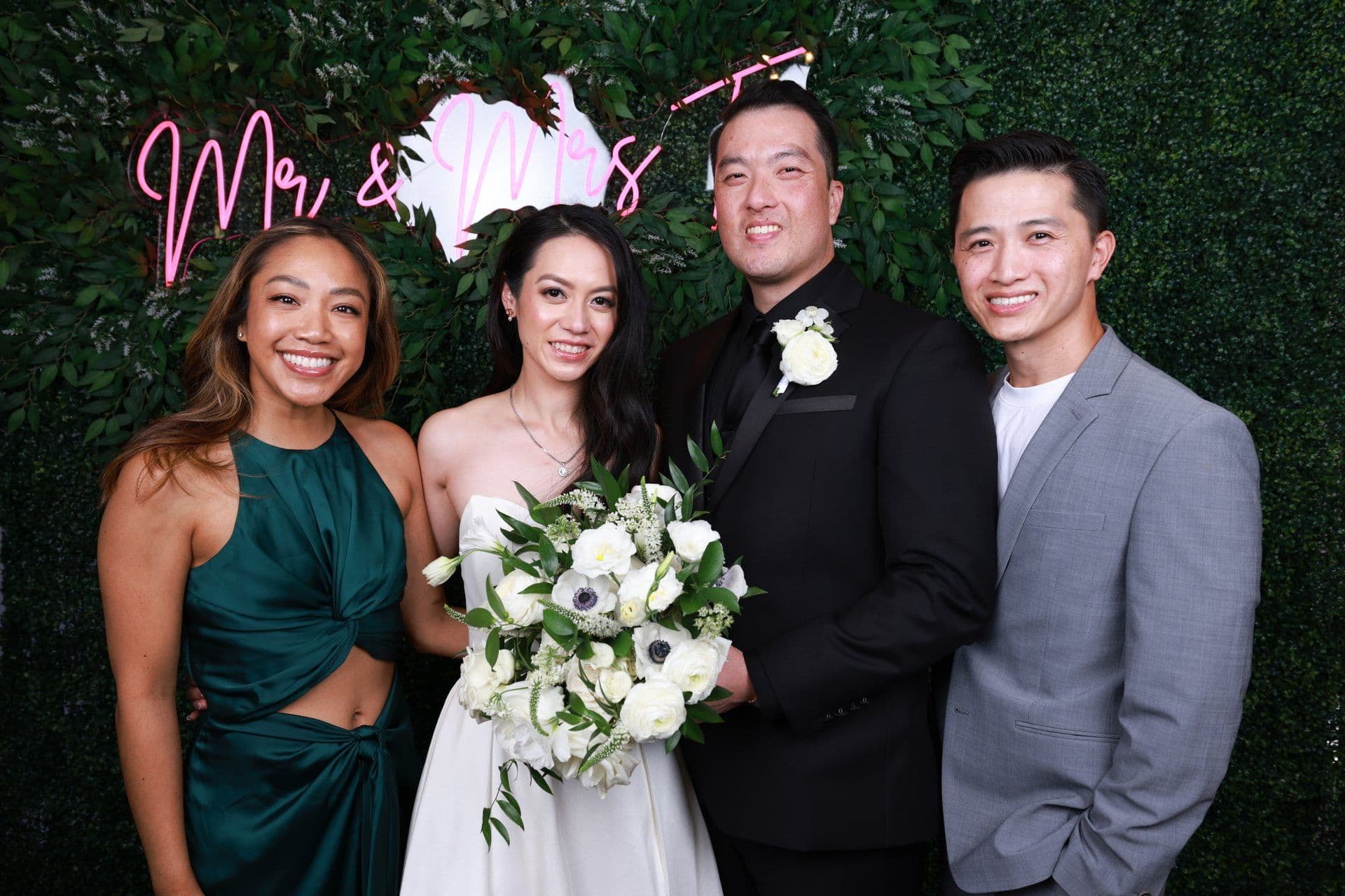 A newlywed couple celebrating with the Radiate Productions team in front of a pink neon wall